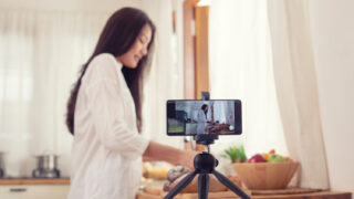 キッチンでスマートフォンと三脚を使って料理動画を撮影している女性