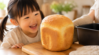 ホームベーカリーで焼いた食パンを見て笑顔になる女の子とミトンをはめたママの手